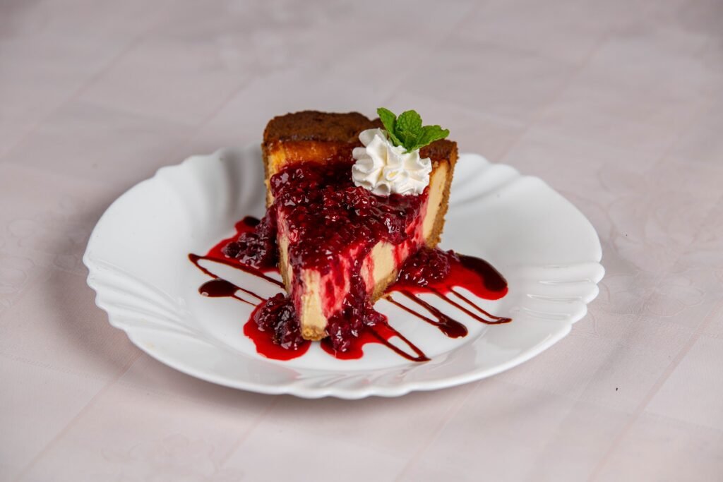 A close-up of a raspberry cheesecake slice with raspberry sauce and mint garnish.