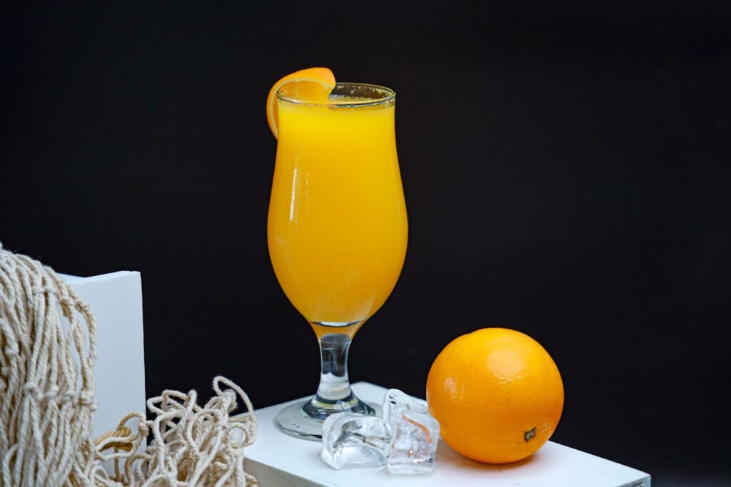 Fresh orange juice served in a glass with ice and a whole orange on a black background.