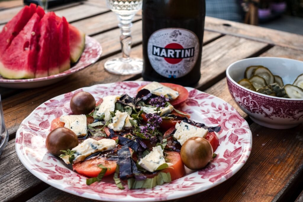 Vibrant garden salad with cheese, surrounded by watermelon, pickles, and wine on a rustic table.
