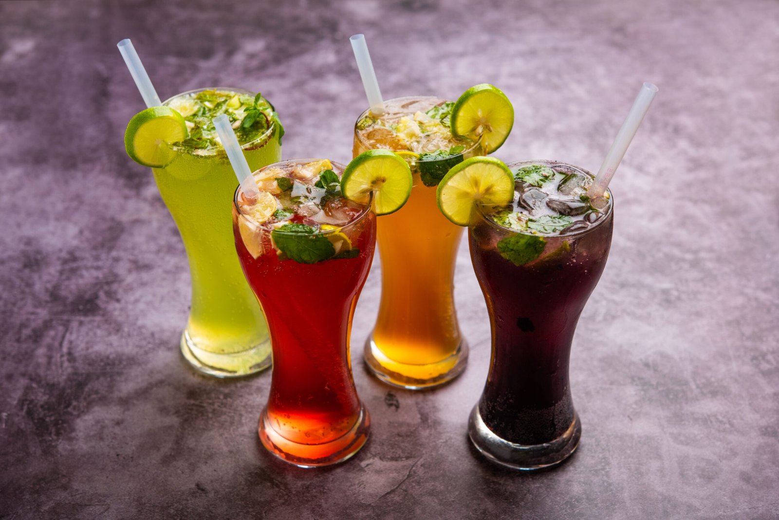 Four vibrant lemon and mint garnished drinks served in tall glasses with straws.