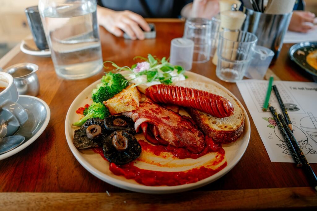 A hearty English breakfast featuring sausages, bacon, toast, and vegetables served on a wooden table at a cozy café.