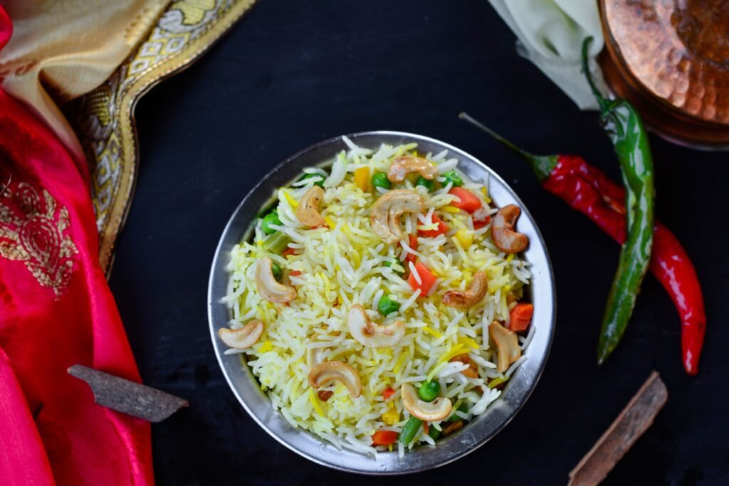 A vibrant, colorful Indian fried rice dish with cashews, chilies, and vegetables in a metal bowl.
