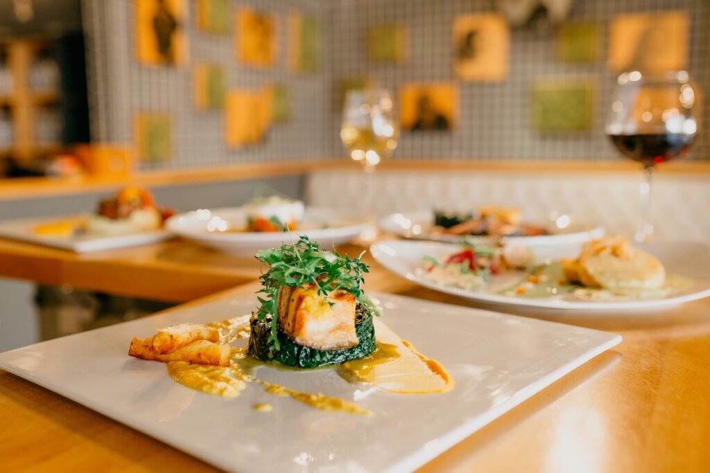 Various appetizing dishes served on white plates and glasses of wine on wooden table in modern light restaurant